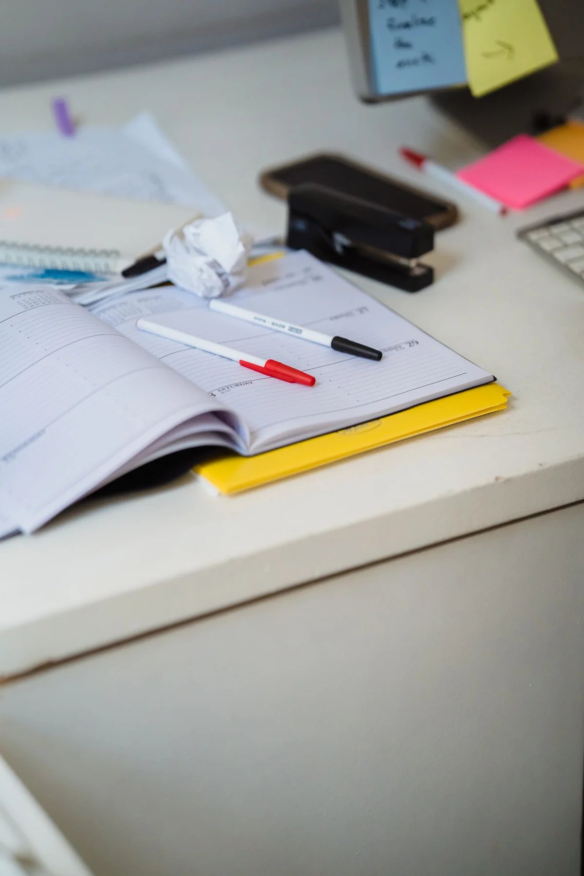 An open weekly planner with pens on a desk.
